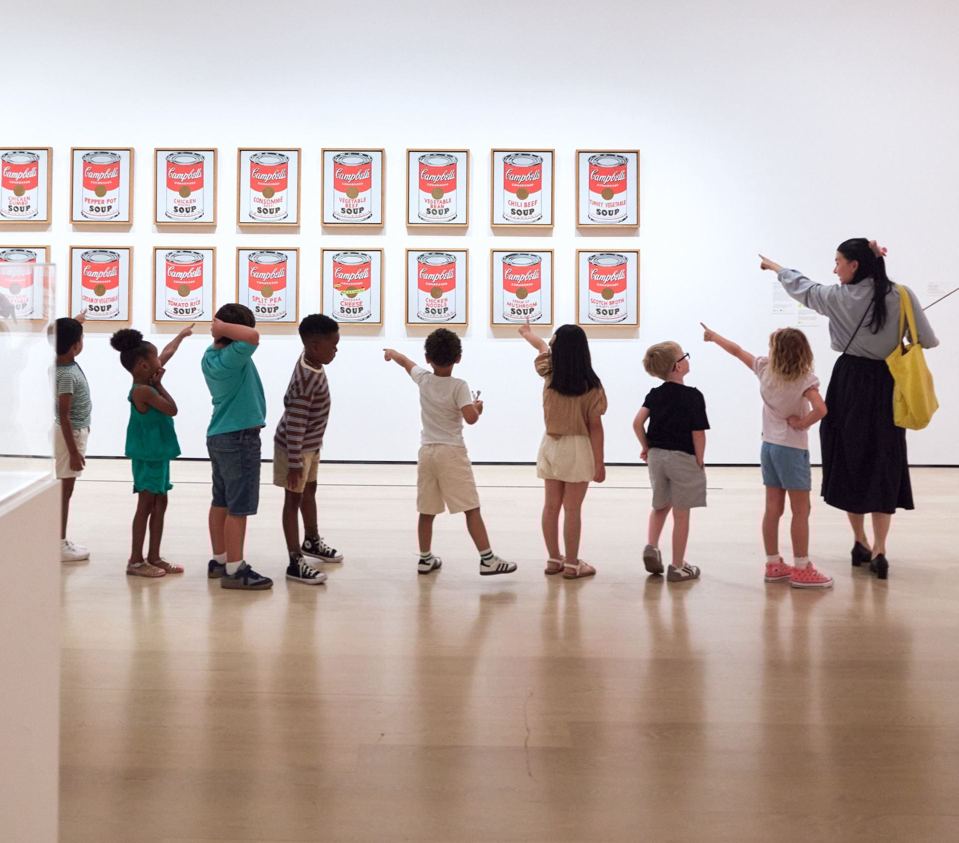 a museum educator leading a line of small children in front of Campbell Soup Can paintings by Andy Warhol.
